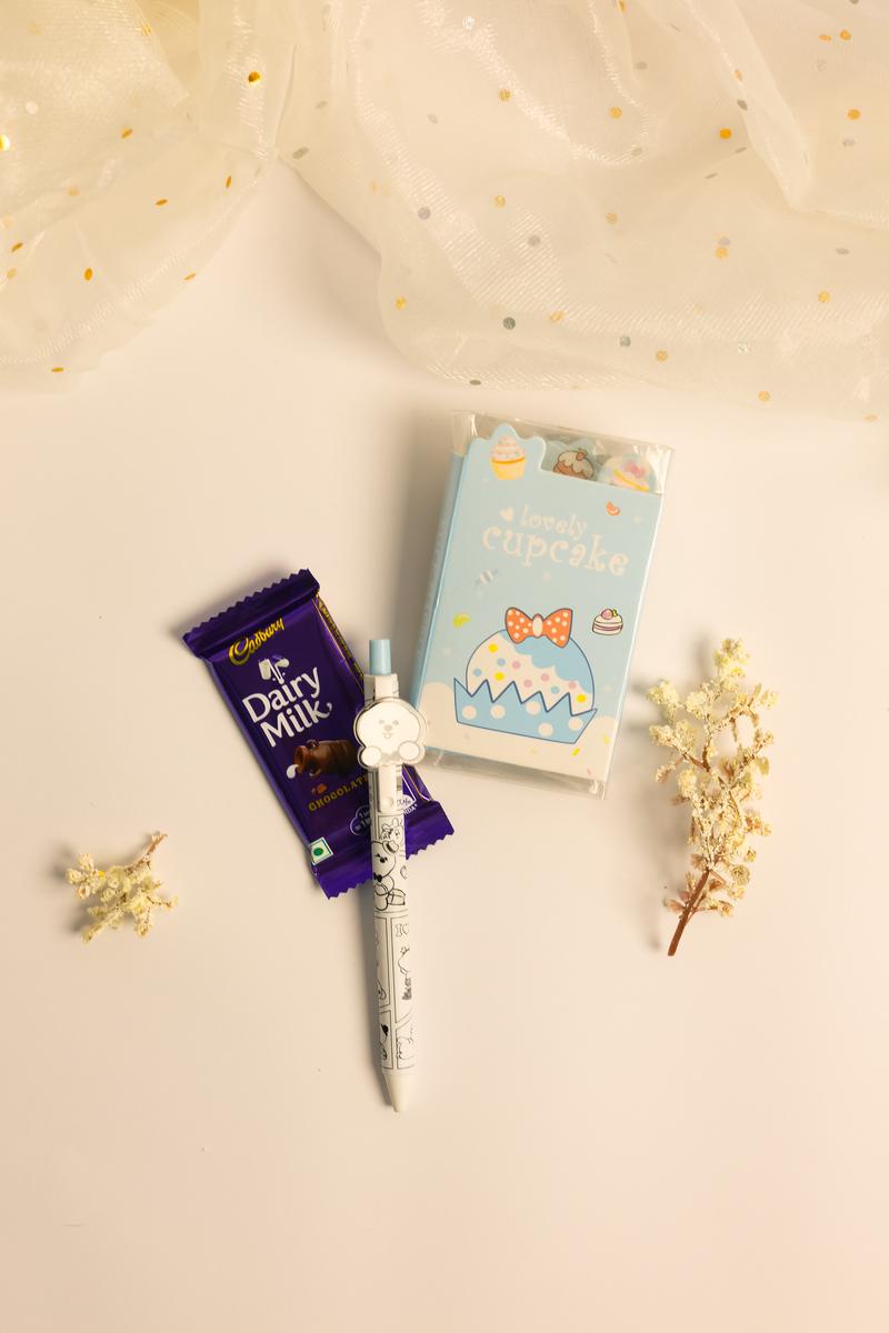 Dairy Milk chocolate bar, a pen, and a small box on a beige surface with decorative elements.